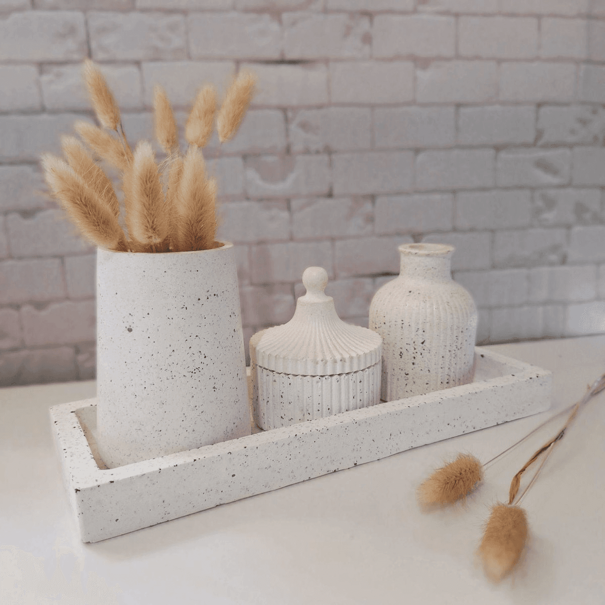 Imagem de um conjunto de vasos e bandeja em concreto branco com acabamento em granilite preto. O conjunto contém uma bandeja redonda e dois vasos redondos de tamanhos diferentes