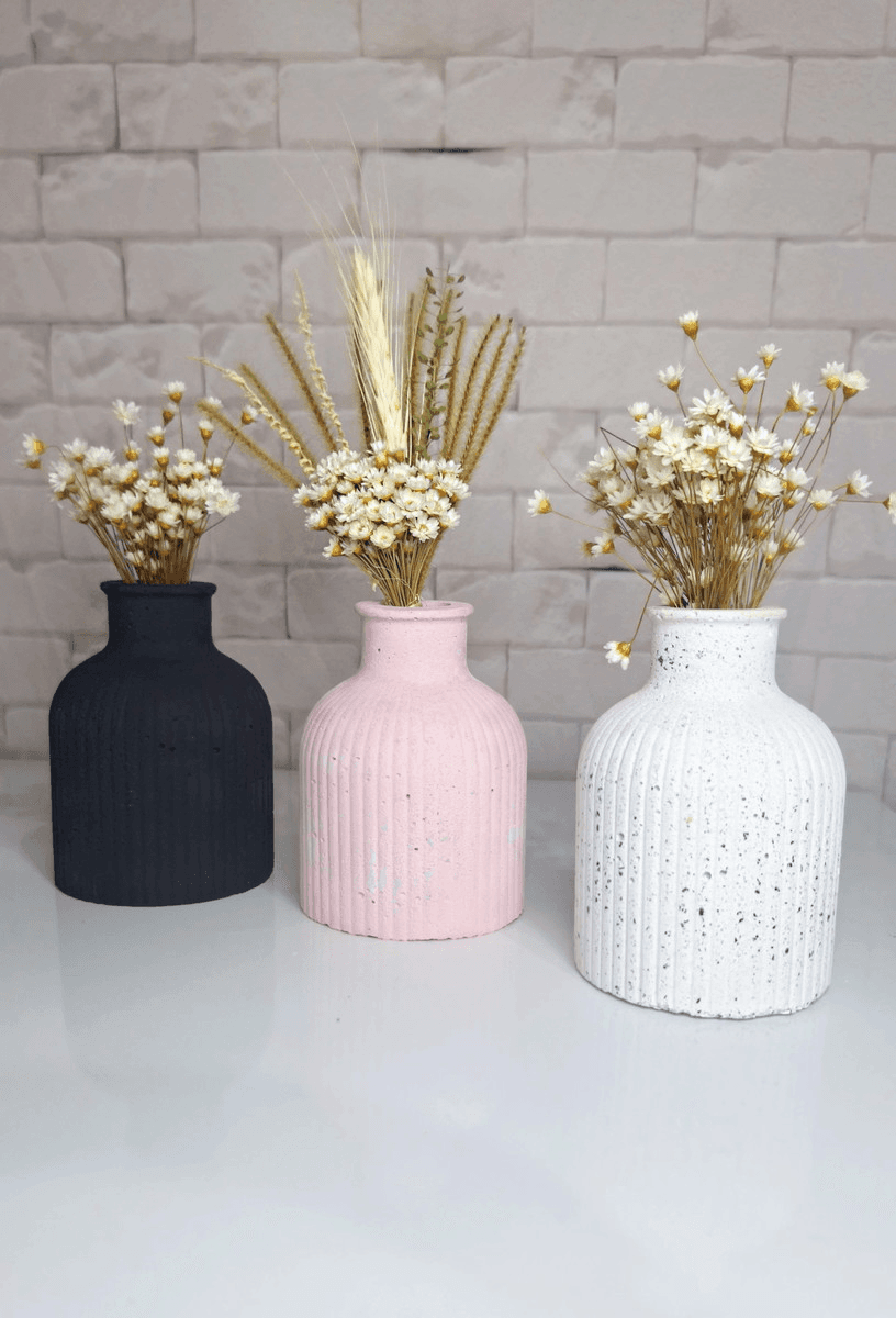 Imagem de 3 vasos de concreto coloridos nas cores rosa, preto e branco